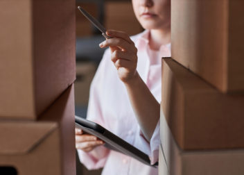 Gros plan d'une jeune femme avec un stylo et une tablette pointant vers l'un des colis