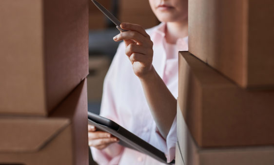 Gros plan d'une jeune femme avec un stylo et une tablette pointant vers l'un des colis