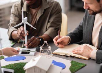 Des gens autour d'une table dont un qui écrit sur un cahier et un autre qui manipule une éolienne miniature